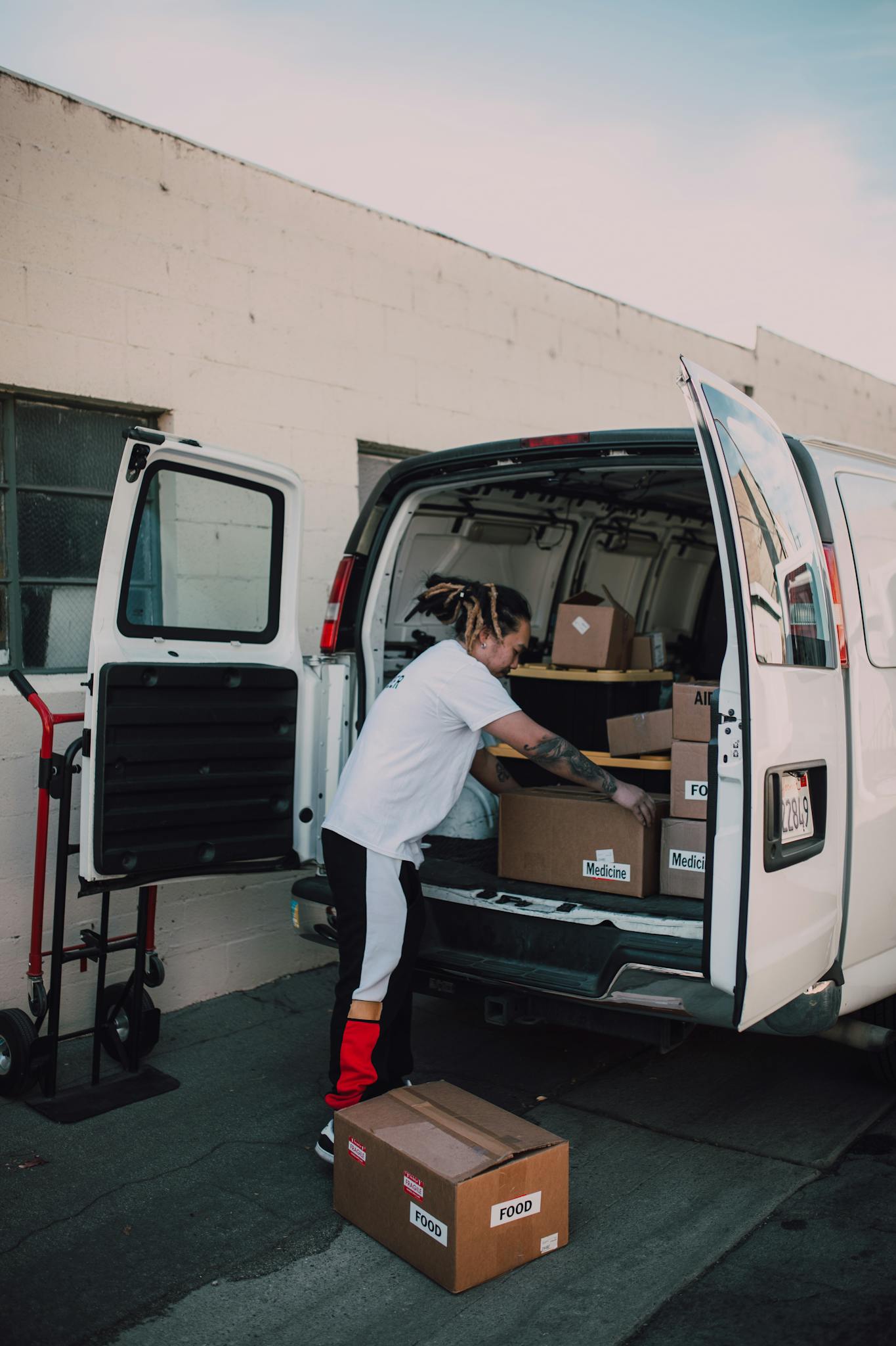 Tattooed volunteer arranging donation boxes in an open van, exuding community spirit outdoors.
